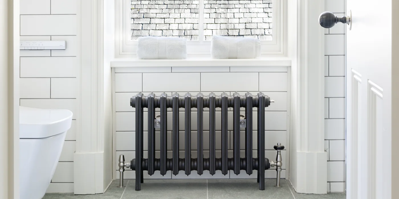 Cast iron column radiator under a window in a white-tiled bathroom