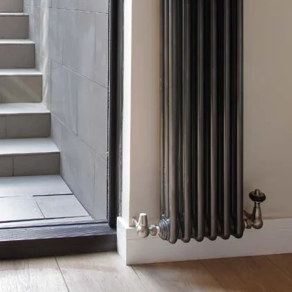 Tall Castrads Florence steel column radiator in a dark finish beside a staircase