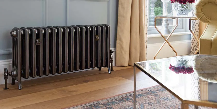 Castrads Grace cast iron radiator in a polished finish beneath a window in a pale blue drawing room