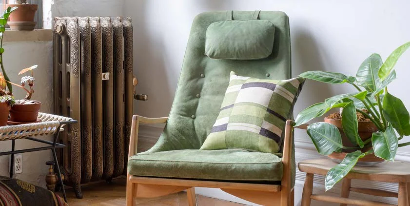 Castrads Rococo ornate cast iron radiator in an aged bronze finish beside a green armchair