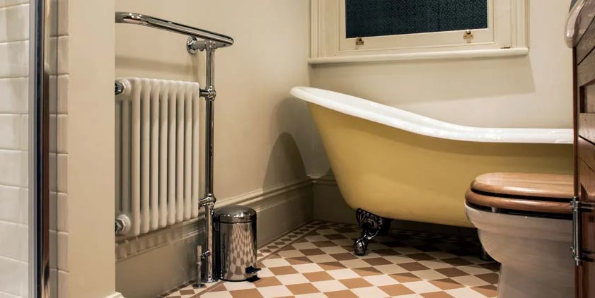 Castrads Vivien traditional towel radiator with chrome hanging bar beside a roll-top bath