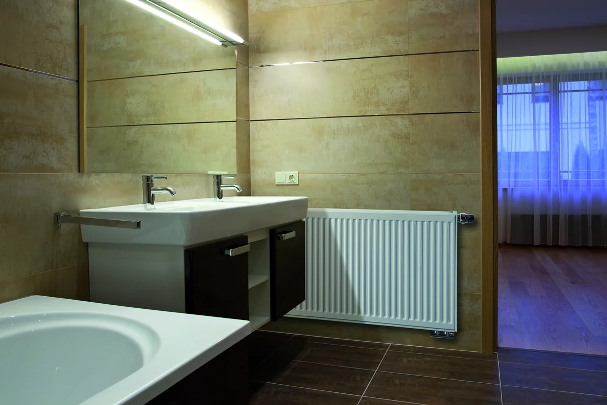 Brugman steel panel radiator on a tiled bathroom wall beside a twin basin