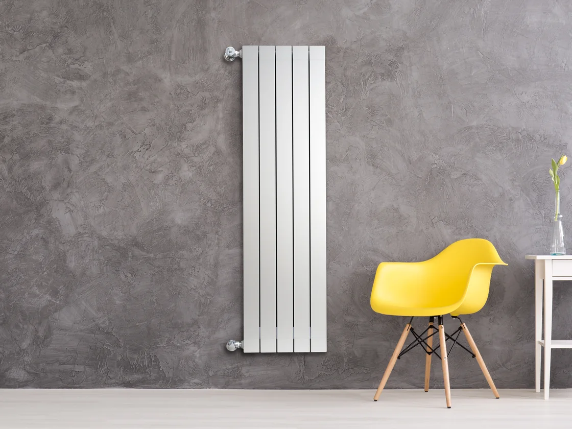 Fondital Blitz Garda vertical aluminium radiator on a grey plastered wall beside a yellow chair